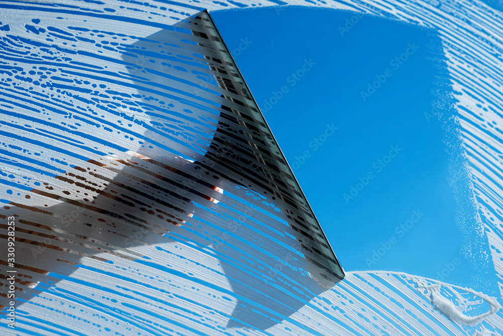 Cleaning soapy windows with squeegee against sunny blue sky. Spring house cleaning concept. Copy space.