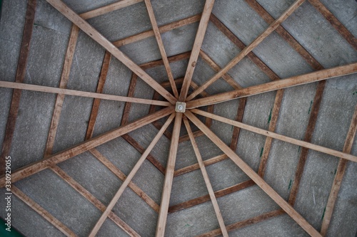 The electric light is in the middle of a hexagon-shaped wooden roof railing frame  photographed at close range from below.