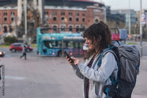 Adventurous female traveler with travel backpack looking at a map on the smartphone