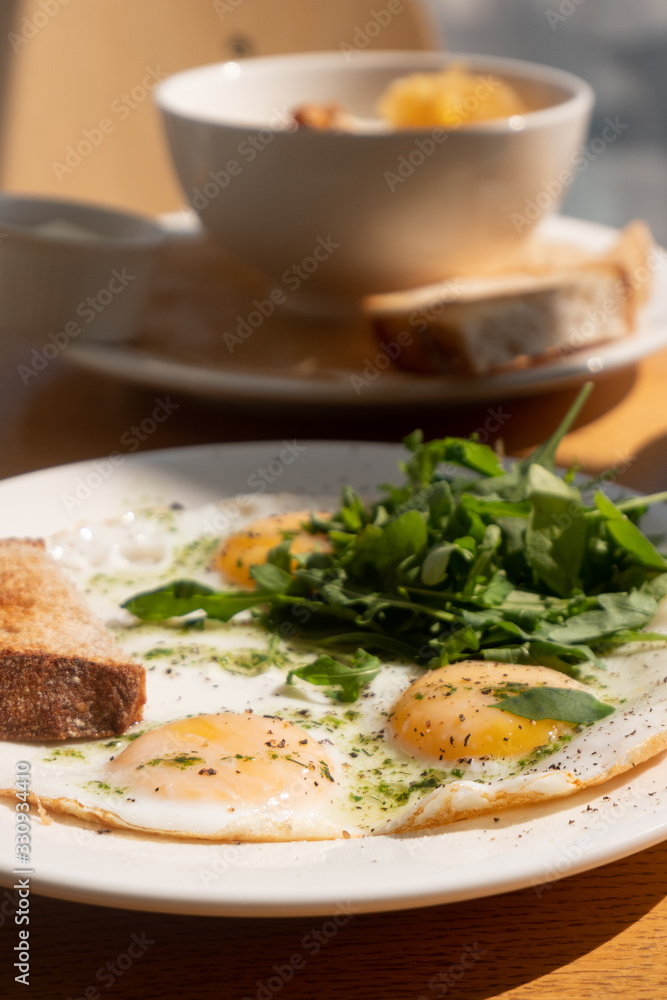 Tasty healthy breakfast: fried eggs, salmon, arugula and croutons on a white plate and a mug of cappuccino on a wooden table. Tasty healthy breakfast: fried eggs, salmon, arugula and croutons on a white plate and a mug of cappuccino on a wooden table.