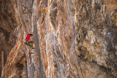 A strong man climbs a beautiful orange rock.