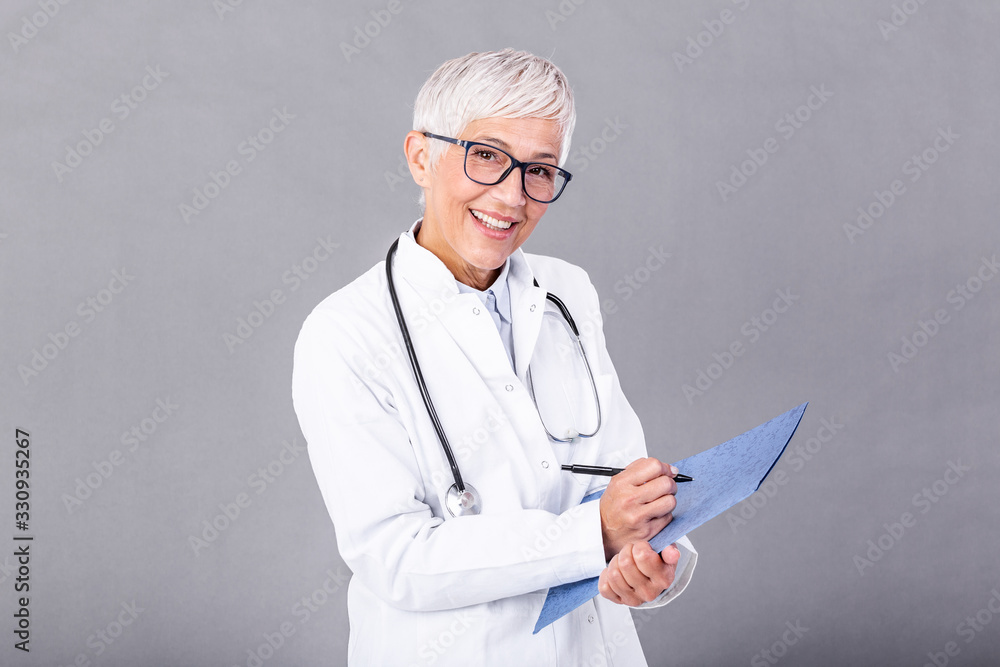 Happy smiling senior female doctor writing on clipboard, isolated on background. Medicine and health care concept. Smiling mature medical doctor woman with stethoscope. Happy smiling senior female doctor writing on clipboard, isolated on background. Medicine and health care concept. Smiling mature medical doctor woman with stethoscope.