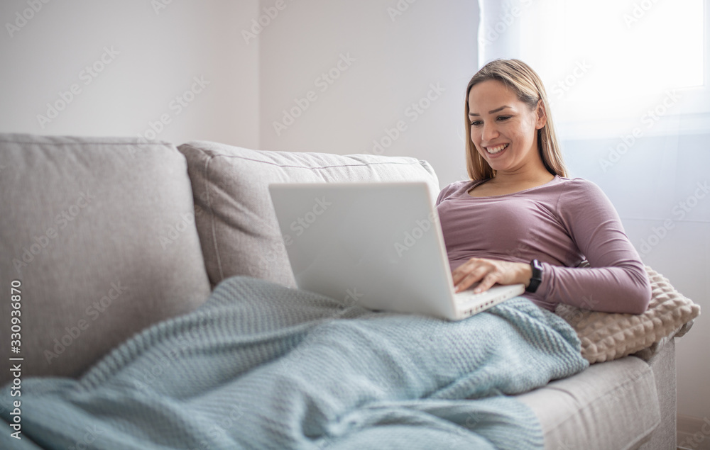 Woman using laptop on a home couch. Woman surfing on line or working from home concept Woman using laptop on a home couch. Woman surfing on line or working from home concept