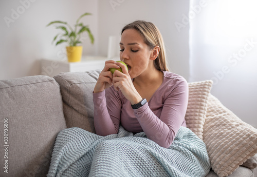 Young attractive woman sitting in sofa, eating apple. Healthy life concept
