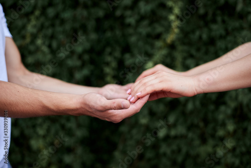 Arms of young couple in love, embracing. Close-up picture of romantic couple hands holding together in front of green leaves wall in summer. Romantic relationship. Valentines day © Natalia