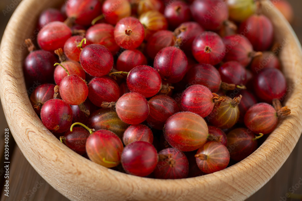 Red gooseberry in a bowl on wooden surface Red gooseberry in a bowl on wooden surface