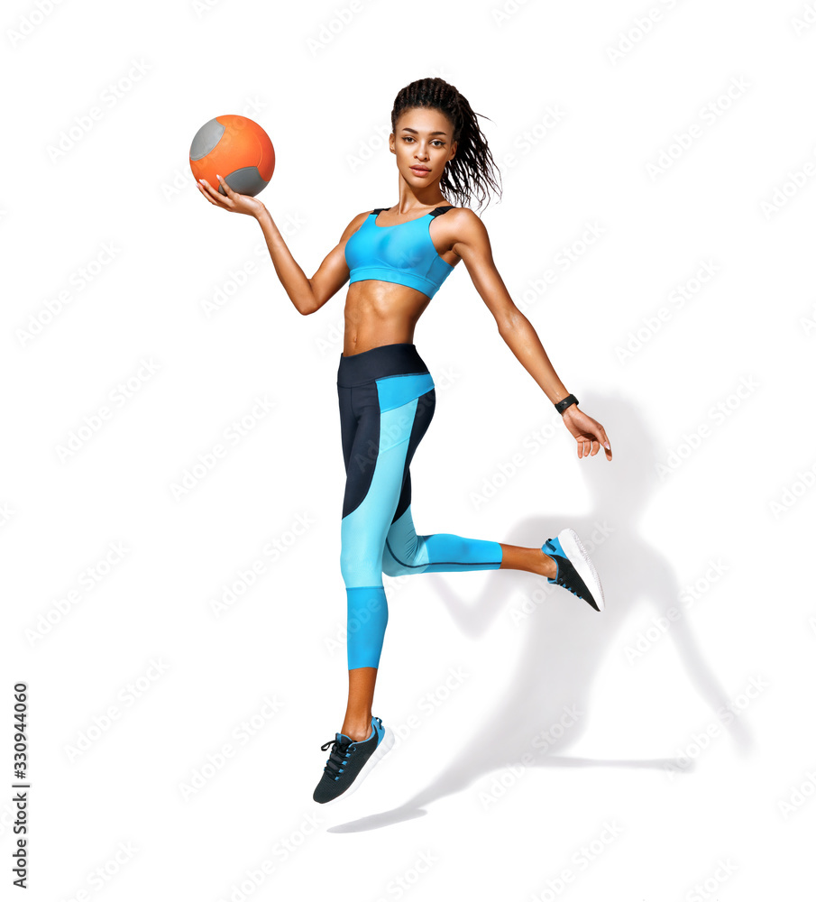 Sporty girl with medicine ball in motion. Photo of african american girl in fashionable sportswear on white background. Dynamic movement. Side view. Full length. Sports and healthy lifestyle