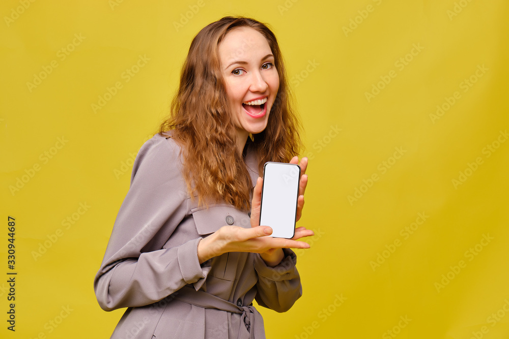 Stylish caucasian girl in a gray dress on a yellow background. Holding a smartphone in his hands and smiles. Copy space. Stylish caucasian girl in a gray dress on a yellow background. Holding a smartphone in his hands and smiles. Copy space.
