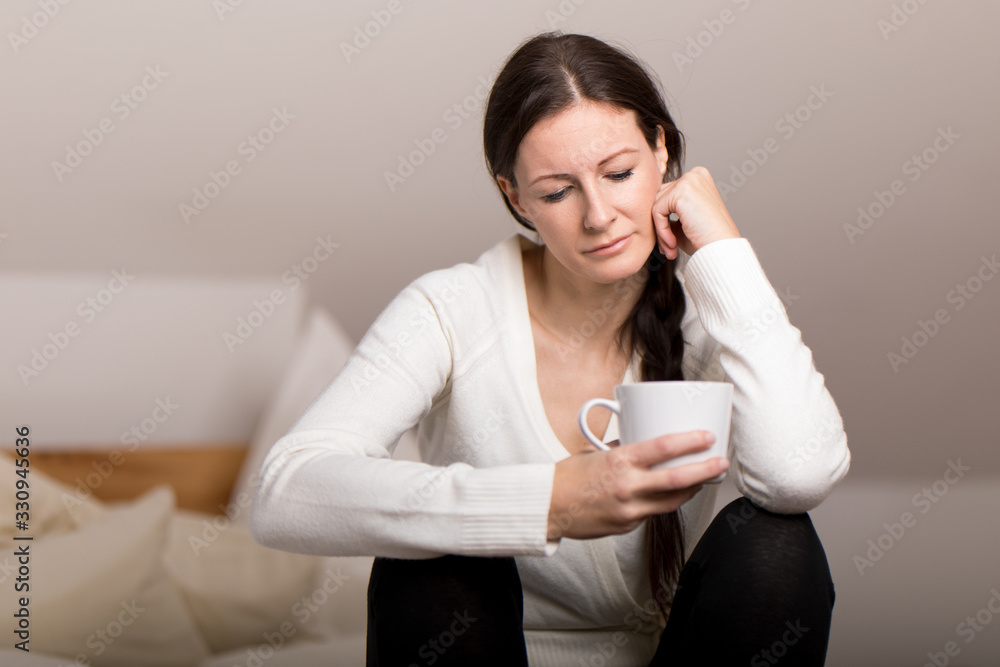 nachdenkliche Frau sitzt mit Kaffeetasse am Bett nachdenkliche Frau sitzt mit Kaffeetasse am Bett