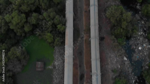 Pan up drone shot of a long pipeline in a mangrove forrest to a busy costal city