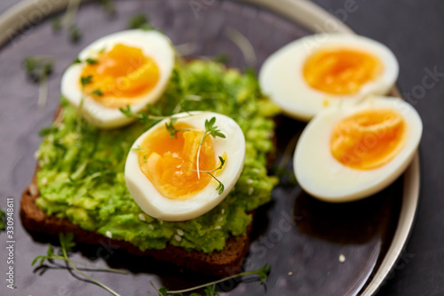 food, eating and breakfast concept - toast bread with mashed avocado, eggs and greens on ceramic plate