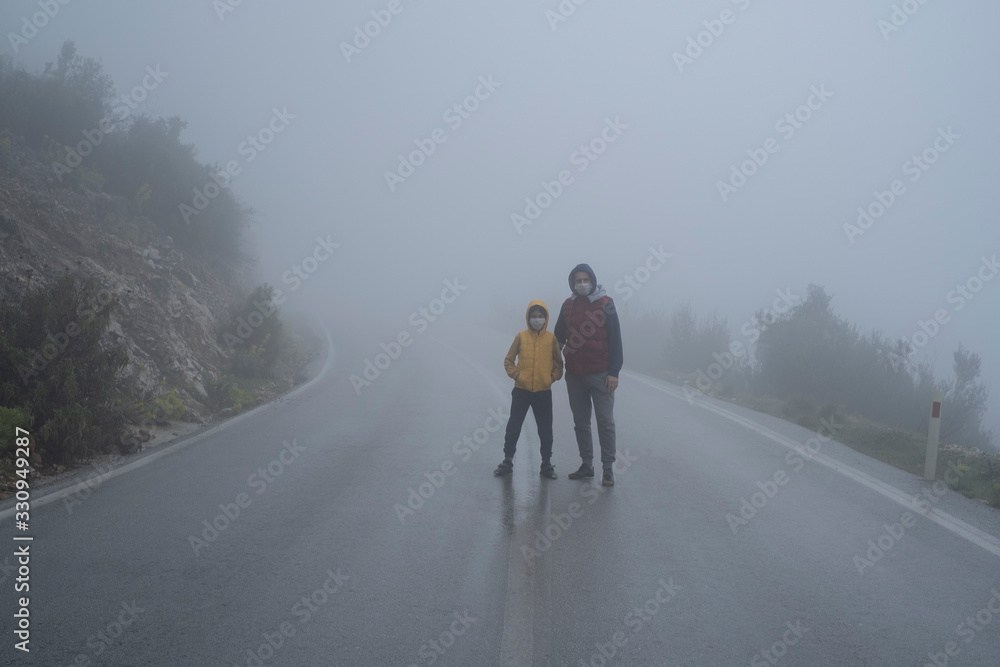 Father and son is standing in the middle of an abandoned road with their face mask that wore for virus protection in foggy weather.