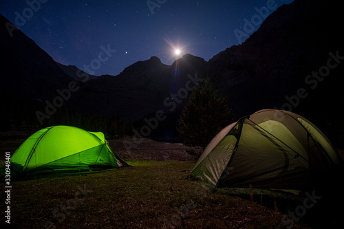 a couple of camp tents illuminated from the inside in a mountain with the light of the moon. 