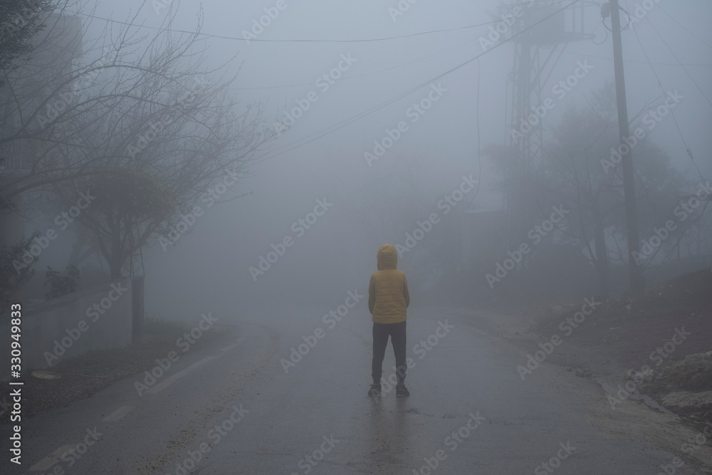 A facing back hoody boy hands in pocket, standing in an abondoned road in air pollution, foggy weather