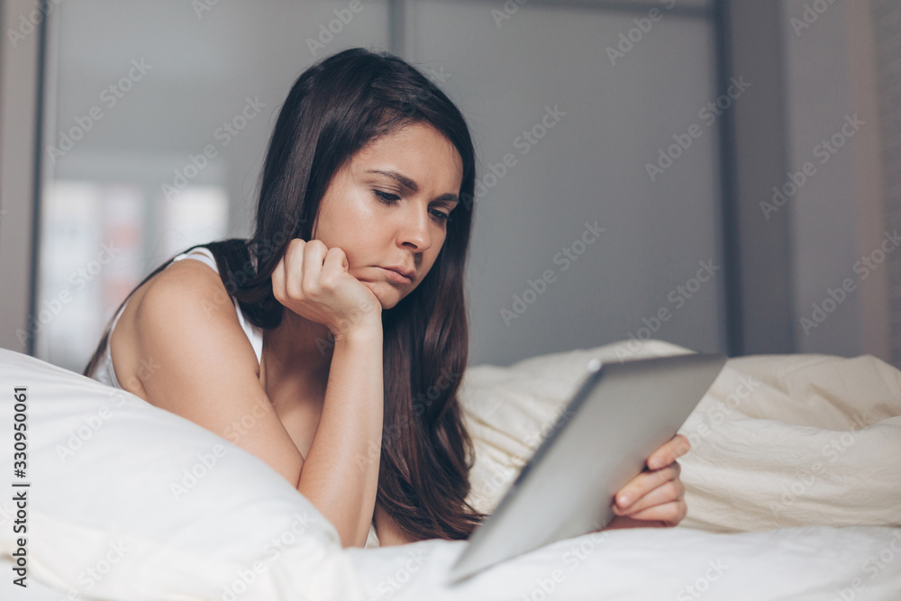 Sad girl looks into tablet in hands on bed Sad girl looks into tablet in hands on bed