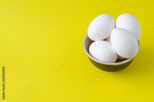 Chicken eggs in bowl on yellow background with copy space
