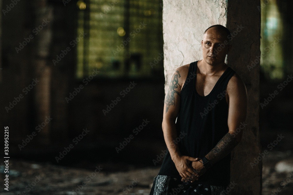a rapper guy stands at a post in an abandoned factory