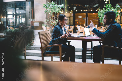 Smart colleagues chatting while working at table in lobby