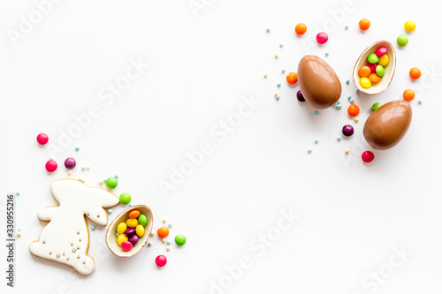 Sweet Easter symbols - chocolate eggs and bunny gingerbread - on white background top-down frame copy space