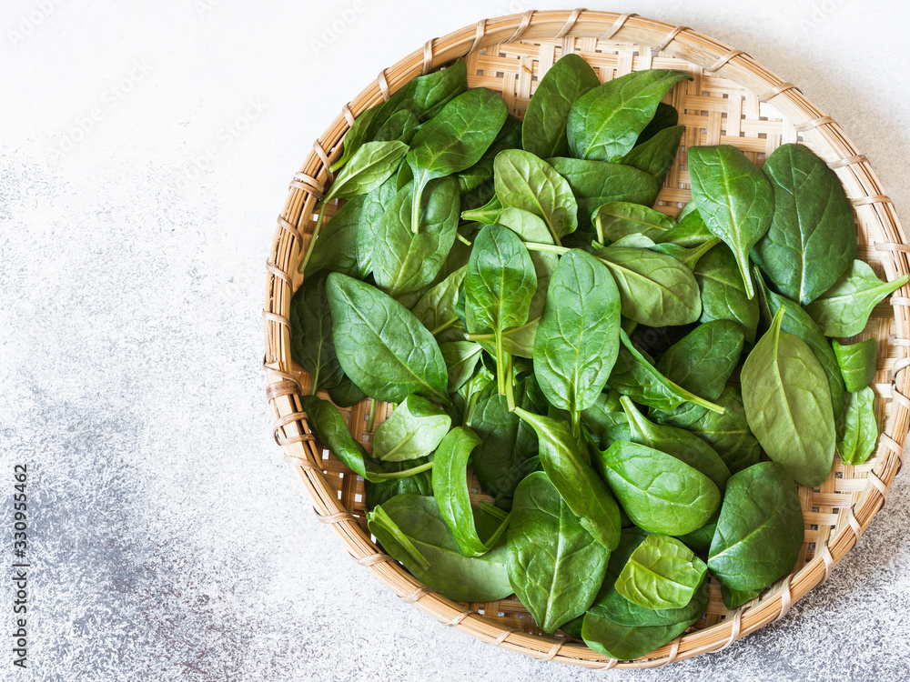 Bamboo wicker tray with fresh spinach on gray background. Top view. Copy space