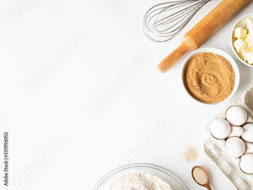 Frame of various baking ingredients - flour, eggs, sugar, butter, dry yeast, and kitchen utensils on white background. Top view. Copy space