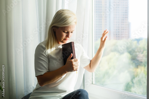 Religious faithful middle aged woman praying with hope faith holding hands clasped together in namaste at home in morning, old mature lady believer christian saying worship prayer with eyes closed