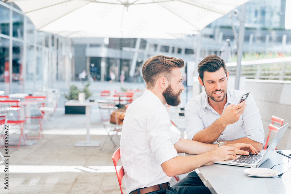 Two beautiful young businessmen sitting bar using computer and smartphone Two beautiful young businessmen sitting bar using computer and smartphone