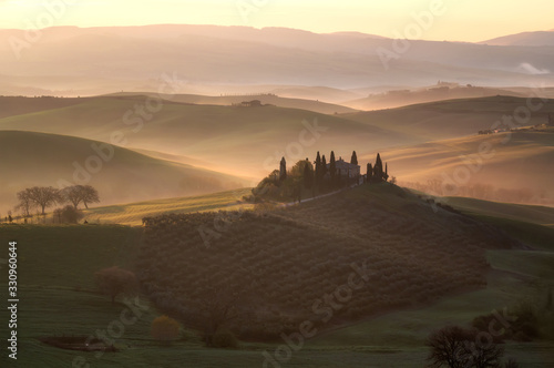 Amazing spring landscape with green rolling hills and farm housе in the heart of Tuscany in morning haze