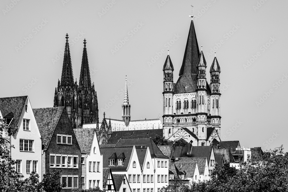 Black and white skyline of the old town with houses rooftops, the tower of the Cologne gothic cathedral and the tower of Gtreat St. Martin church in Cologne, North Rhine Westphalia, Germany