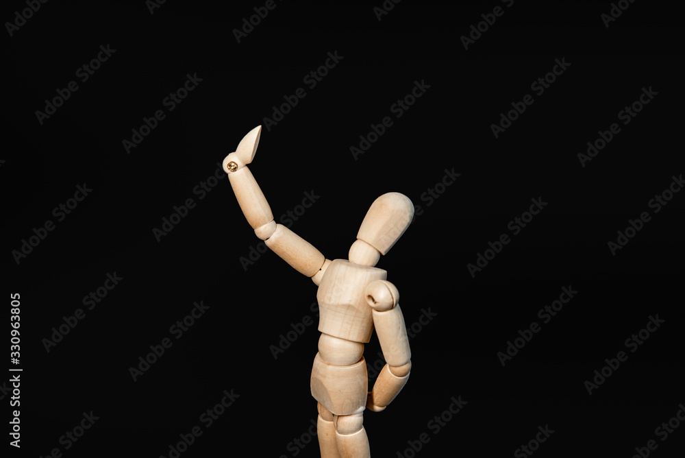 the wooden figure raised its hand high, as if looking into a mirror or taking a selfie, proudly admiring itself against a black background the wooden figure raised its hand high, as if looking into a mirror or taking a selfie, proudly admiring itself against a black background
