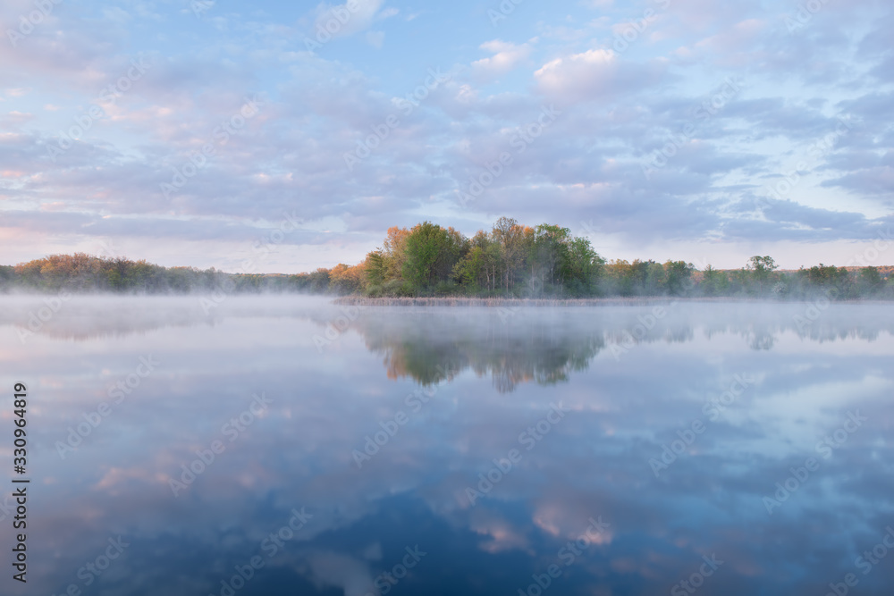 Fototapeta premium Landscape at sunrise of the foggy, spring shoreline of Whitford Lake with reflections in calm water, Fort Custer State Park, Michigan, USA