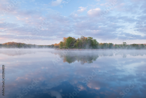 Landscape at sunrise of the foggy, spring shoreline of Whitford Lake with reflections in calm water, Fort Custer State Park, Michigan, USA