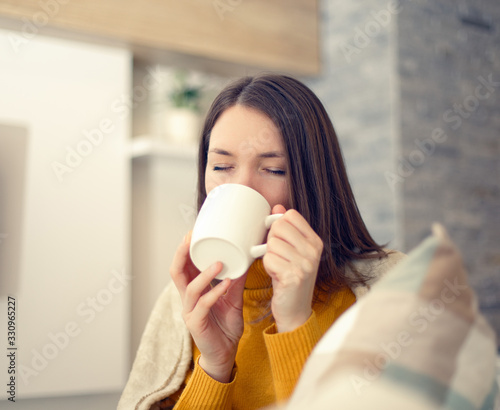 Ill young woman with flu virus at home drinking tea 