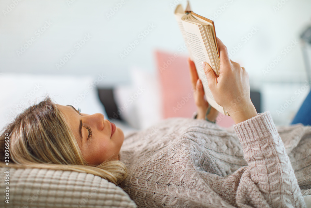 Young woman lies on her back in bed reading a book - obrazy, fototapety, plakaty 