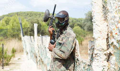 Paintball player in camouflage standing with gun after paintball match