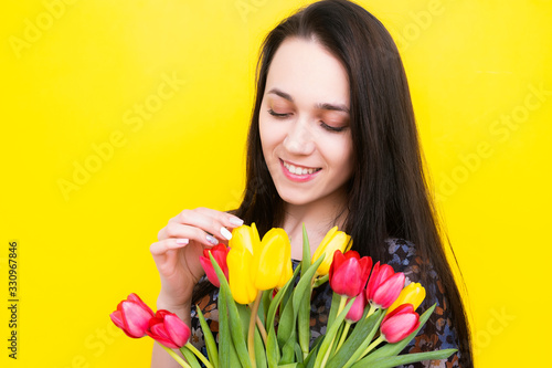 Brunette with a bouquet of tulips on a yellow background. Young woman with flowers. Women's Day.