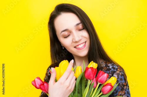 Happy Woman with a bouquet of tulips smiling closing her eyes on a yellow background. Mothers Day.