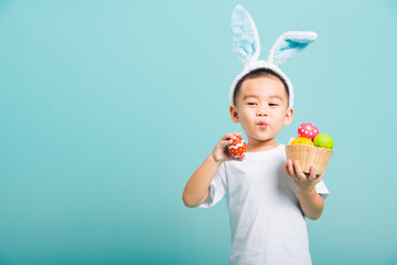 little child boy smile wearing bunny ears and white T-shirt, hold basket with full Easter eggs