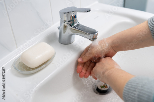 Two hands washing in a white sink