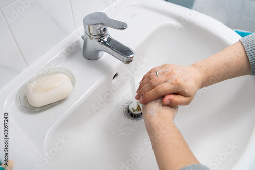 two hands washing with soap in a white sink