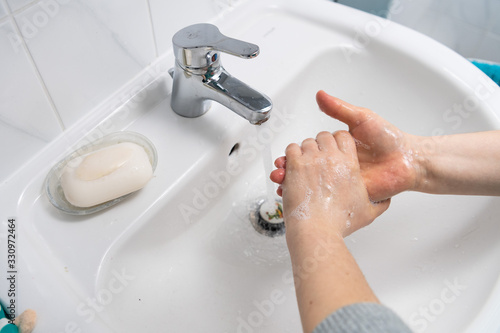 two hands washing with soap in a white sink