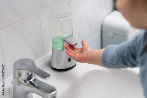 infant using a soap dispenser on a white sink