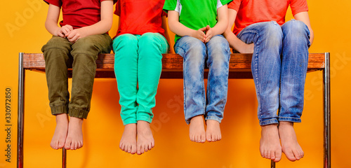 Billede på lærred Children in bright and colorful clothes sit barefoot with their legs dangling to the bottom