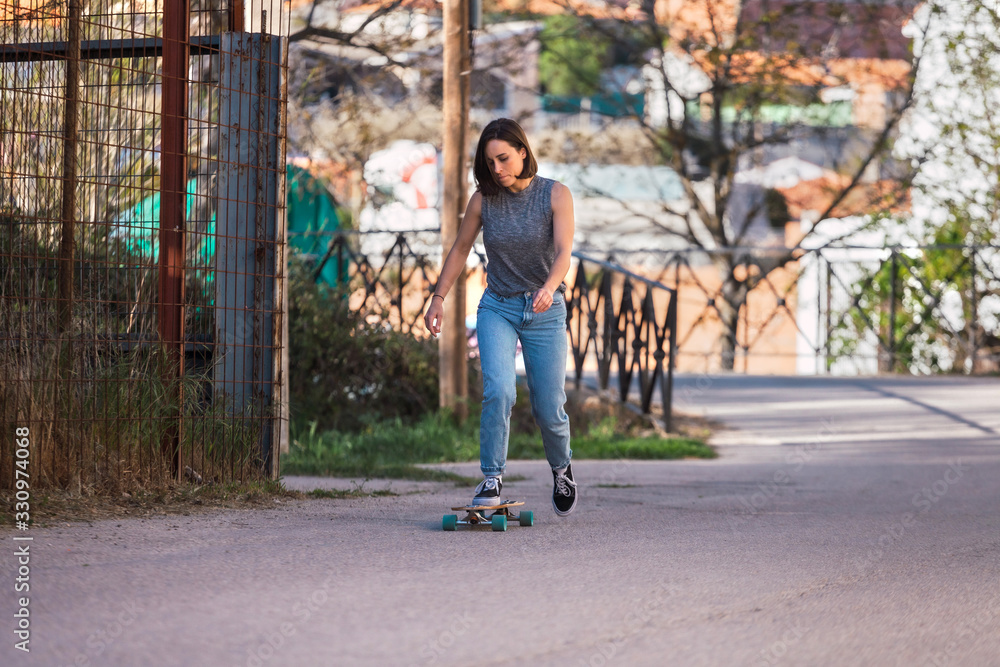 Obraz premium Young skater woman riding on her longboard in the village