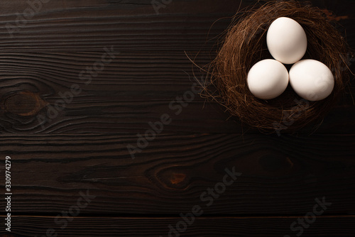 top view of white chicken eggs in brown nest on dark wooden background