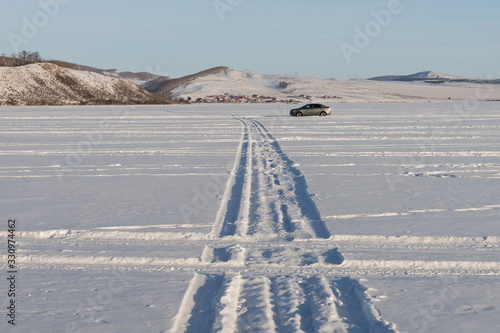 A geometric pattern from the wheels of cars was imprinted on the snowy plain of a lake against the shore.
