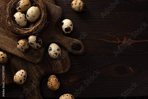 top view of quail eggs in nest and on brown cutting boards on dark wooden surface