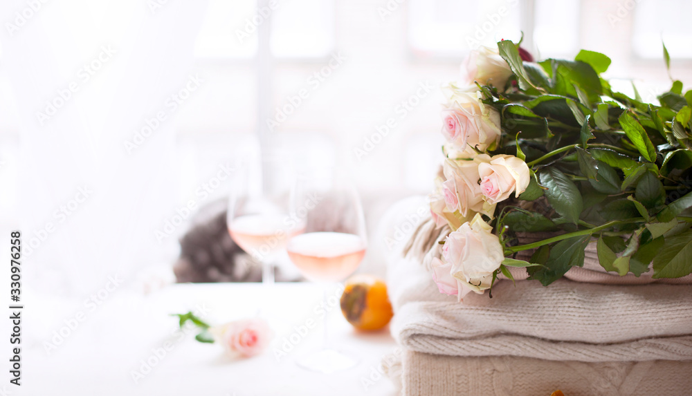 Bouquet of roses natural light. Flowers by the window and two glasses of rose wine. Cozy and romantic atmosphere. Banner long format. Copy space. Selective focus shifted from the subject.