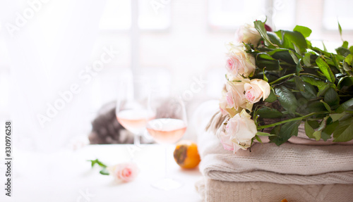Bouquet of roses natural light. Flowers by the window and two glasses of rose wine. Cozy and romantic atmosphere. Banner long format. Copy space. Selective focus shifted from the subject.