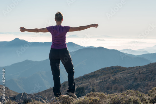 Hiker woman with open arms in cross on top of the mountain.